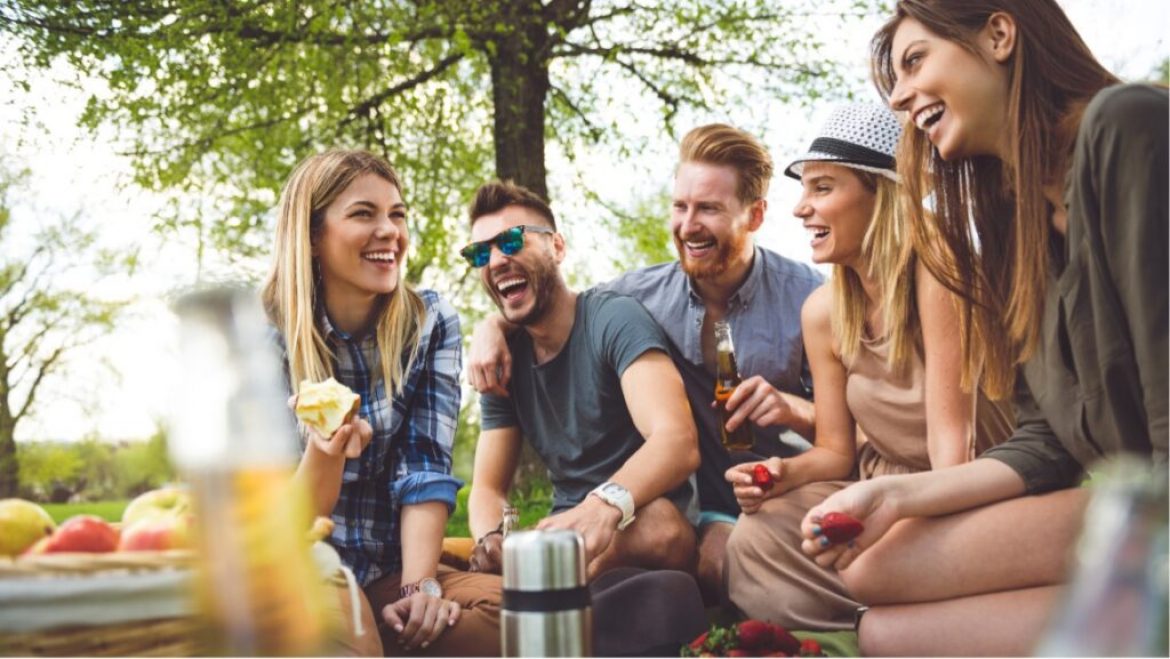 People sitting on lawn and laughing while eating and drinking